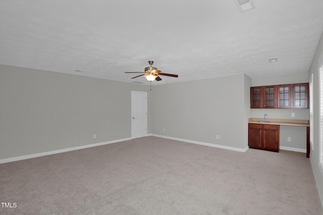 unfurnished living room with a ceiling fan, baseboards, light carpet, and bar with sink