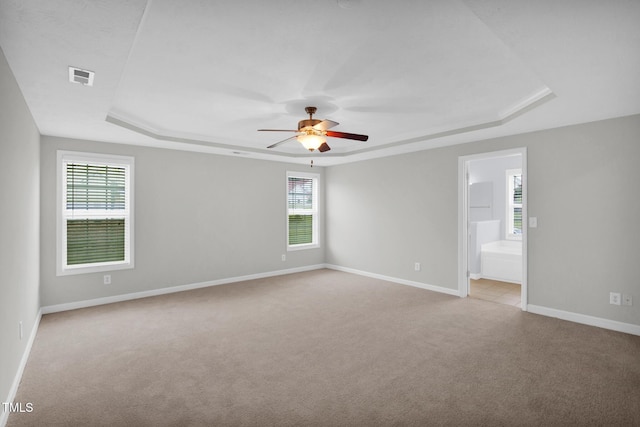 spare room featuring a tray ceiling, light carpet, plenty of natural light, and ceiling fan