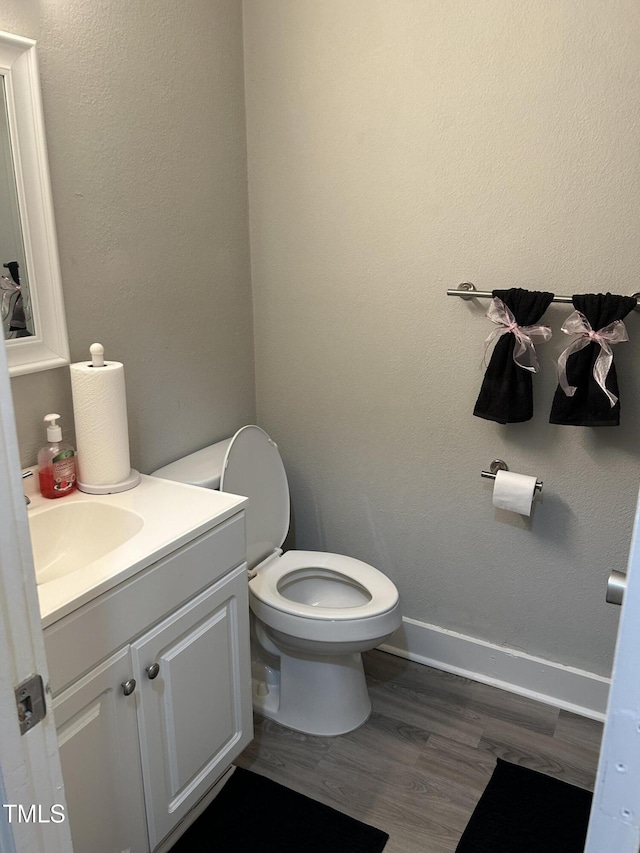half bath featuring wood finished floors, vanity, toilet, and baseboards