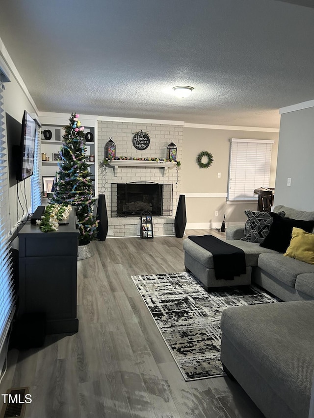 living area with wood finished floors, ornamental molding, a fireplace, and a textured ceiling