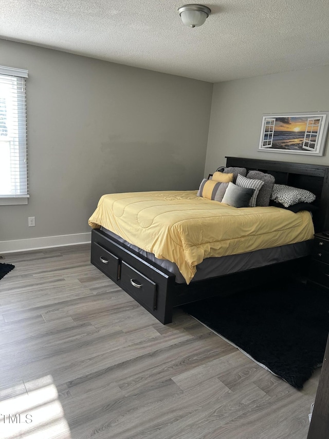 bedroom with light wood finished floors, a textured ceiling, and baseboards
