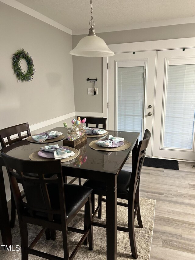 dining space featuring light wood finished floors, ornamental molding, and a textured ceiling