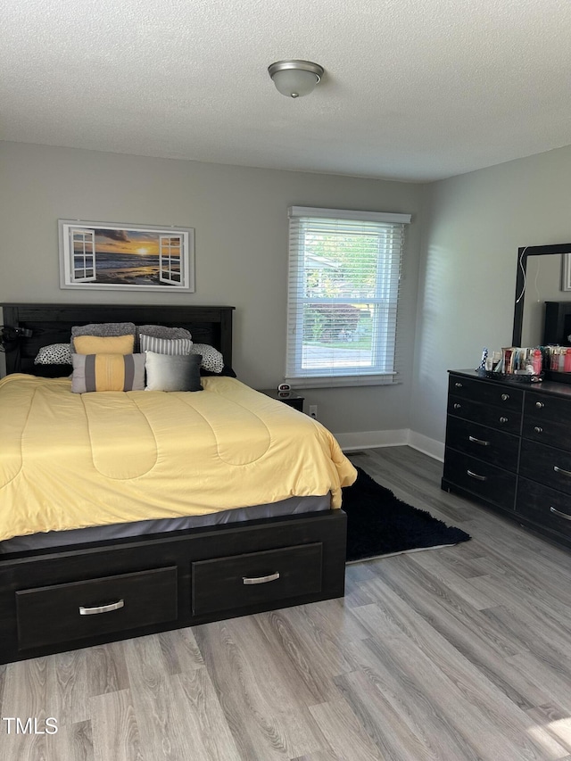 bedroom featuring light wood-type flooring, a textured ceiling, and baseboards