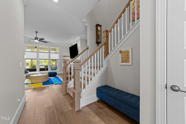 stairway featuring wood finished floors, a ceiling fan, baseboards, crown molding, and recessed lighting