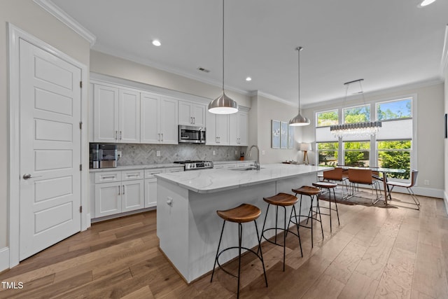 kitchen featuring stainless steel microwave, wood finished floors, white cabinetry, backsplash, and a kitchen island with sink