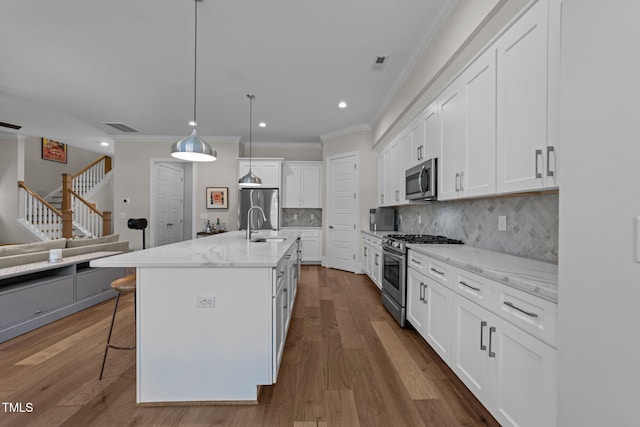 kitchen with appliances with stainless steel finishes, ornamental molding, white cabinetry, decorative backsplash, and a kitchen breakfast bar