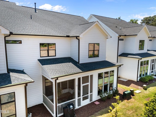 rear view of house with a sunroom and roof with shingles