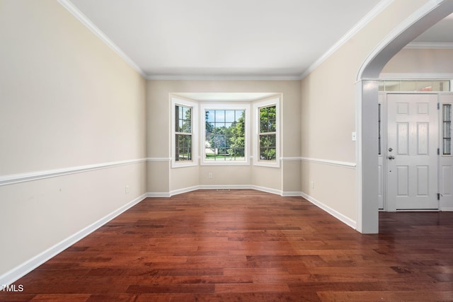 empty room featuring arched walkways, ornamental molding, wood finished floors, and baseboards