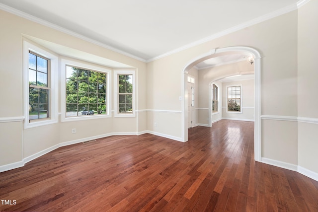 empty room with arched walkways, wood-type flooring, crown molding, and baseboards