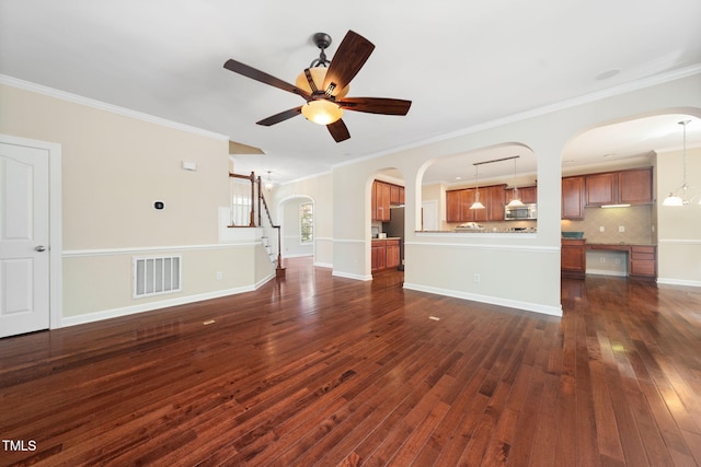 unfurnished living room with arched walkways, crown molding, a ceiling fan, dark wood-style flooring, and stairs