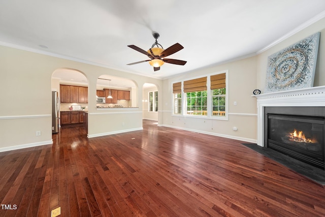 unfurnished living room featuring arched walkways, crown molding, a fireplace with flush hearth, dark wood finished floors, and ceiling fan