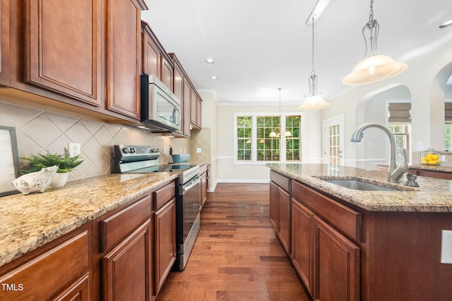 kitchen with appliances with stainless steel finishes, a sink, dark wood finished floors, an island with sink, and decorative backsplash