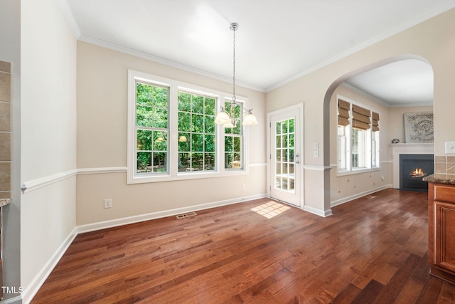 unfurnished dining area with wood finished floors, arched walkways, baseboards, ornamental molding, and a warm lit fireplace