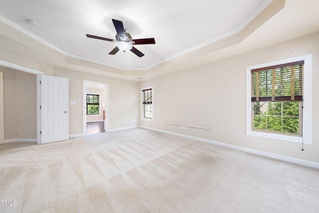unfurnished room with a tray ceiling, crown molding, a ceiling fan, light carpet, and baseboards