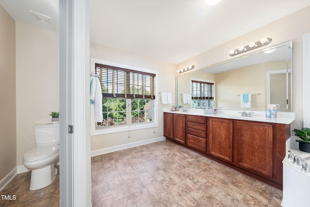 bathroom featuring baseboards, double vanity, and toilet