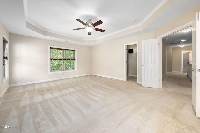 unfurnished bedroom featuring a tray ceiling, light colored carpet, ornamental molding, a spacious closet, and baseboards