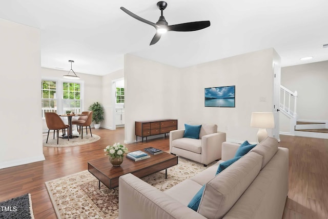 living area with a ceiling fan, wood finished floors, baseboards, and stairs