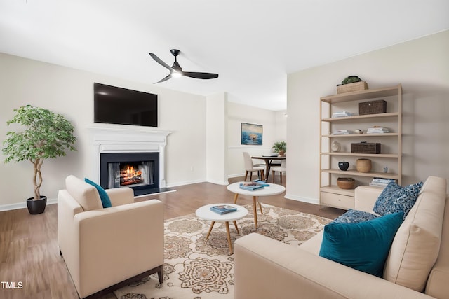 living area featuring a ceiling fan, wood finished floors, a glass covered fireplace, and baseboards