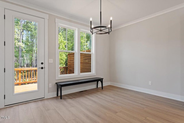 doorway with a chandelier, crown molding, light wood-type flooring, and baseboards