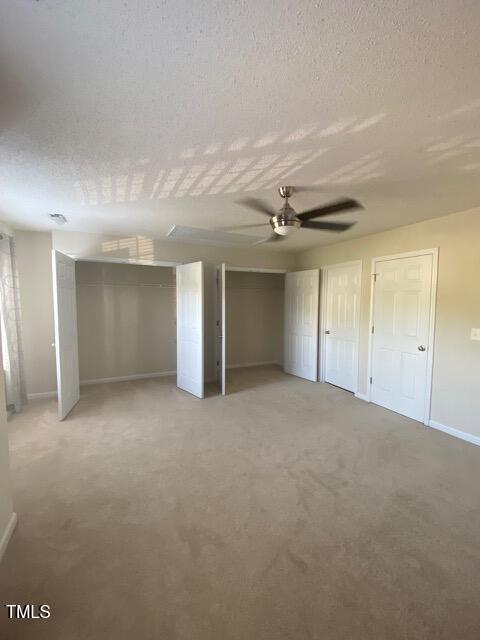 21 Suncrest Ct, Durham, NC 27703 - unfurnished bedroom with multiple closets, baseboards, light carpet, a textured ceiling, and a ceiling fan