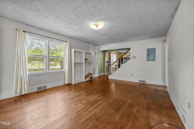 unfurnished living room with wood finished floors, electric panel, stairway, baseboards, and a textured ceiling