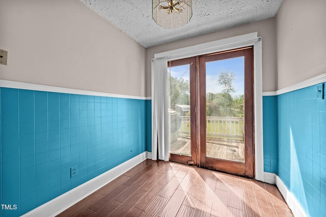 doorway with tile walls, wainscoting, a textured ceiling, and wood finished floors