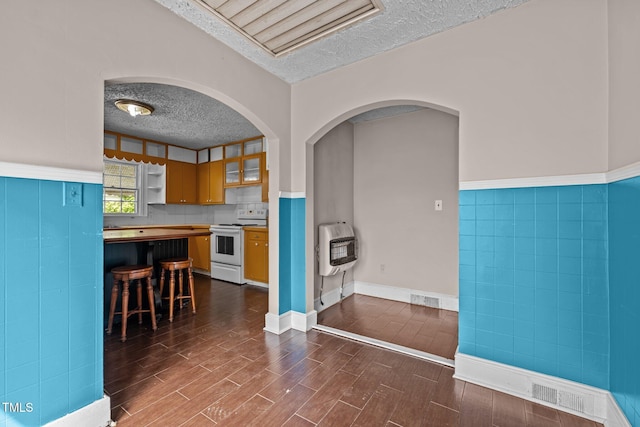kitchen featuring electric stove, heating unit, a textured ceiling, a breakfast bar area, and dark wood-style flooring