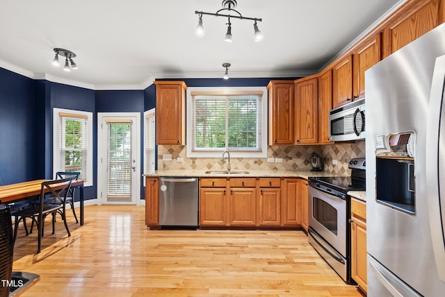 kitchen with stainless steel appliances, a sink, light wood finished floors, light stone counters, and crown molding