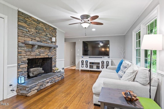 living area featuring ornamental molding, a ceiling fan, wood finished floors, and a stone fireplace