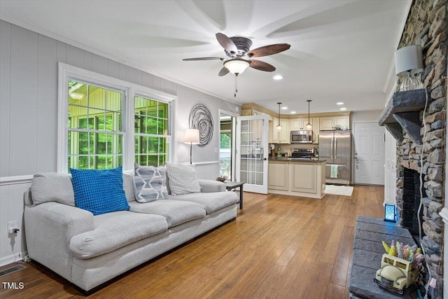 living room with a ceiling fan, a stone fireplace, light wood-style floors, crown molding, and recessed lighting