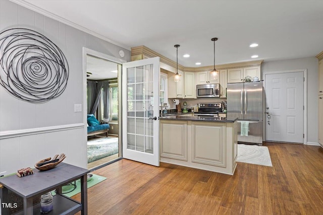 kitchen with stainless steel appliances, wood finished floors, dark countertops, a peninsula, and cream cabinets