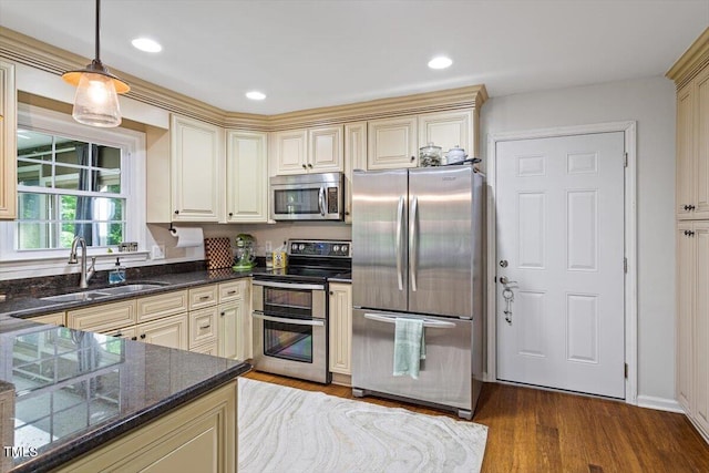 kitchen with appliances with stainless steel finishes, a sink, cream cabinets, wood finished floors, and hanging light fixtures
