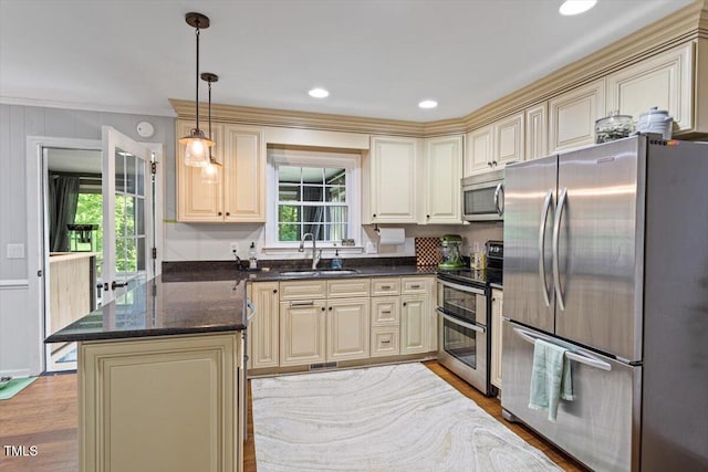 kitchen featuring stainless steel appliances, a sink, ornamental molding, cream cabinetry, and a peninsula