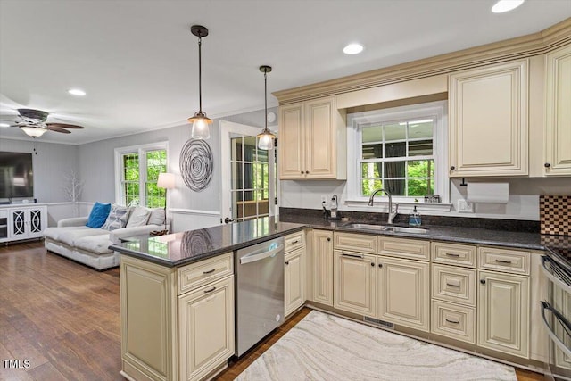 kitchen featuring cream cabinets, stainless steel dishwasher, a sink, open floor plan, and crown molding