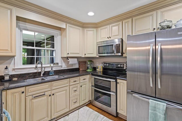kitchen featuring stainless steel appliances, cream cabinetry, a sink, and dark stone countertops