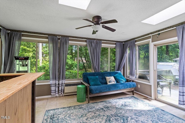 living area featuring a skylight, light tile patterned floors, a textured ceiling, ceiling fan, and baseboards
