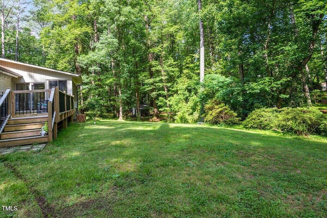 view of grassy yard with a wooden deck and a forest view