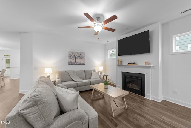 living area with wood finished floors, a glass covered fireplace, ceiling fan, and baseboards