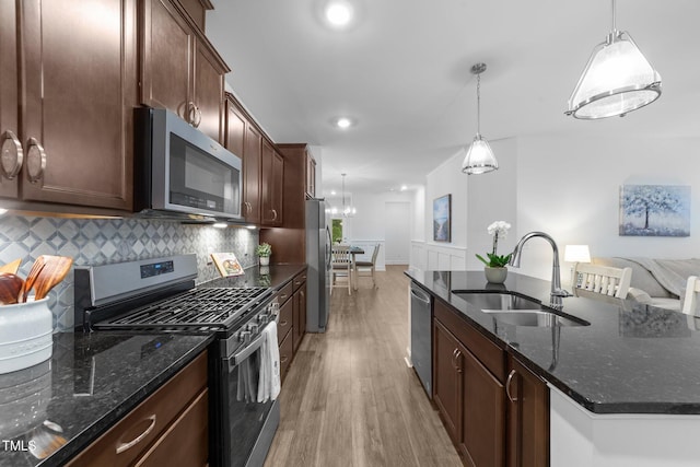 kitchen featuring stainless steel appliances, a sink, light wood finished floors, an island with sink, and tasteful backsplash