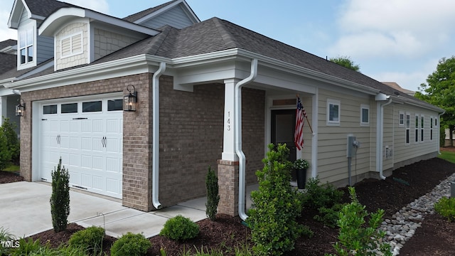 view of property exterior with an attached garage, a shingled roof, concrete driveway, and brick siding