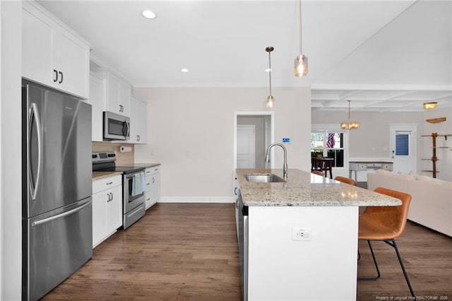 kitchen with stainless steel appliances, a sink, a breakfast bar area, open floor plan, and white cabinetry