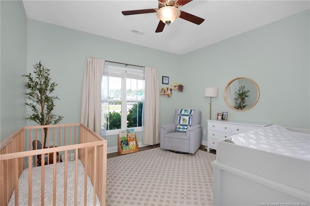 bedroom with a crib, ceiling fan, and light carpet