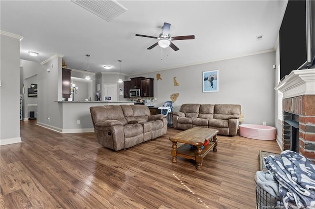 living area featuring crown molding, ceiling fan, wood finished floors, a fireplace, and baseboards