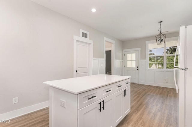 303 Godwin St, Selma, NC 27576 - kitchen with freestanding refrigerator, light wood-style flooring, white cabinets, decorative light fixtures, and a wainscoted wall