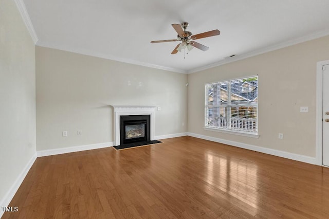unfurnished living room featuring wood finished floors, ceiling fan, ornamental molding, a glass covered fireplace, and baseboards