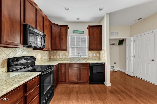 kitchen with black appliances, a sink, wood finished floors, backsplash, and recessed lighting
