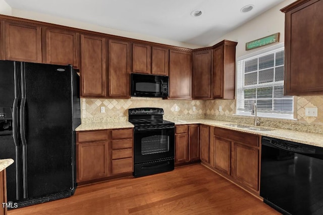 kitchen with black appliances, a sink, wood finished floors, tasteful backsplash, and light stone countertops