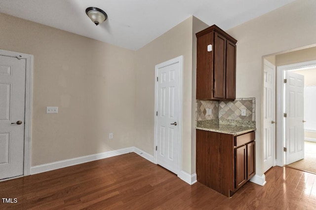kitchen featuring dark wood-style flooring, backsplash, light stone counters, baseboards, and dark brown cabinetry