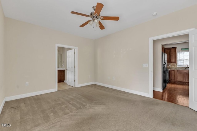 unfurnished bedroom with dark colored carpet, freestanding refrigerator, a sink, ensuite bath, and baseboards