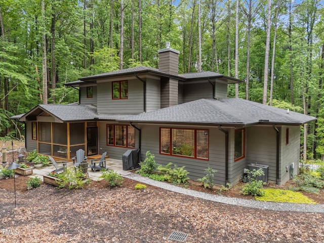 1115 Trailwood Dr, Raleigh, NC 27606 - prairie-style house featuring roof with shingles, a chimney, a patio area, a sunroom, and a view of trees
